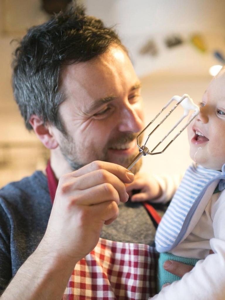 Ein lachender Vater mit kleinem Kind auf dem Arm in der Küche.