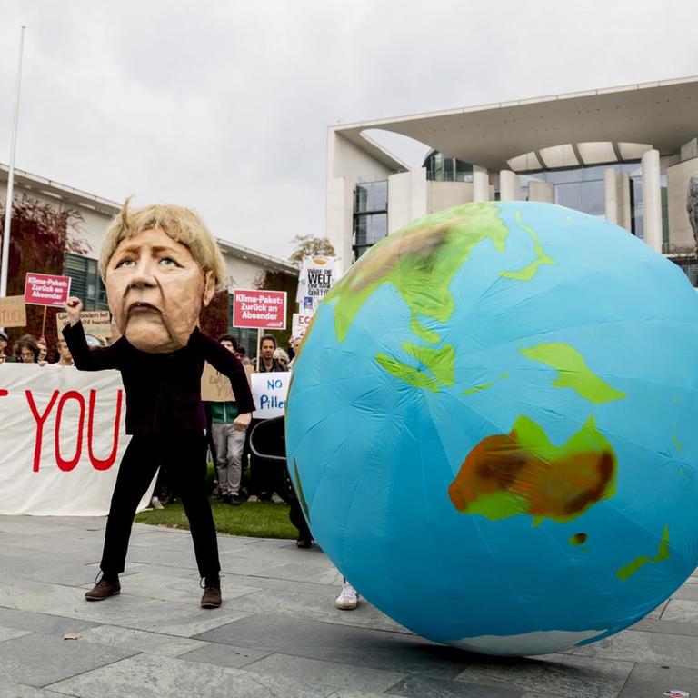 Zwei Darsteller tragen bei einer Kundgebung von Fridays for Future und der Nichtregierungsorganisation Campact Masken, die Bundeskanzlerin Angela Merkel (CDU, M) und Olaf Scholz (SPD, r), Bundesfinanzminister, zeigen. Andere Demonstranten halten ein Banner mit der Aufschrift "How dare you?".