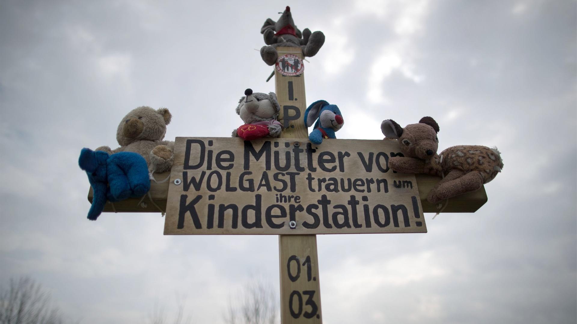 Ein Holzkreuz mit Plüschtieren und dem Schriftzug "Die Mütter von Wolgast trauern um ihre Kinderstadtion!" ist am 29.03.2017 am Ortsrand von Wolgast (Mecklenburg-Vorpommern) zu sehen.
