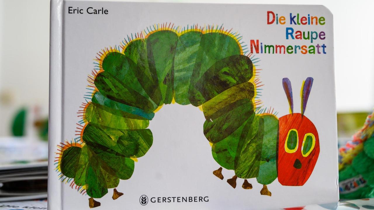 Eine Ausgabe des Buches "Die kleine Raupe Nimmersatt" des Kinderbuchautors Eric Carle steht auf einem Tisch.