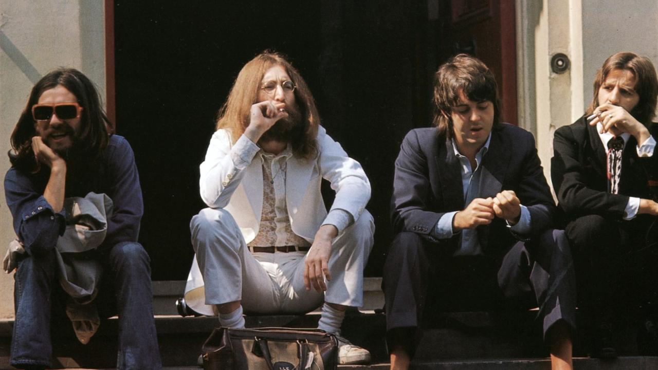 Die Beatles sitzen auf einer Treppe und gucken unverwandt in verschiedene Richtungen.