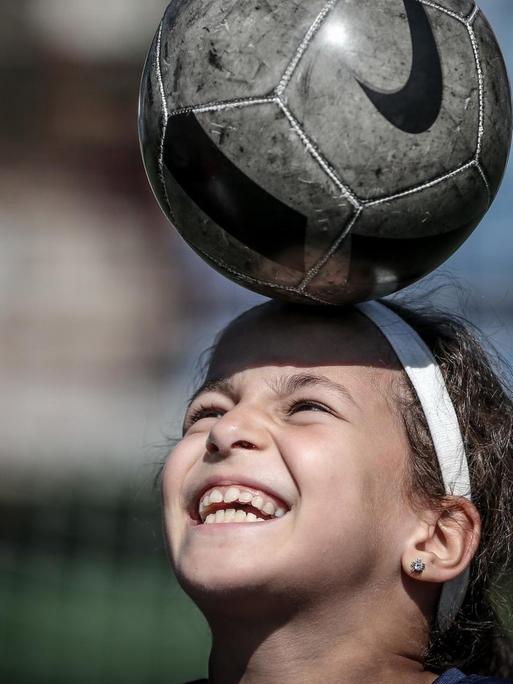 Ein 9-jähriges Mädchen balanciert einen Fußball auf dem Kopf.