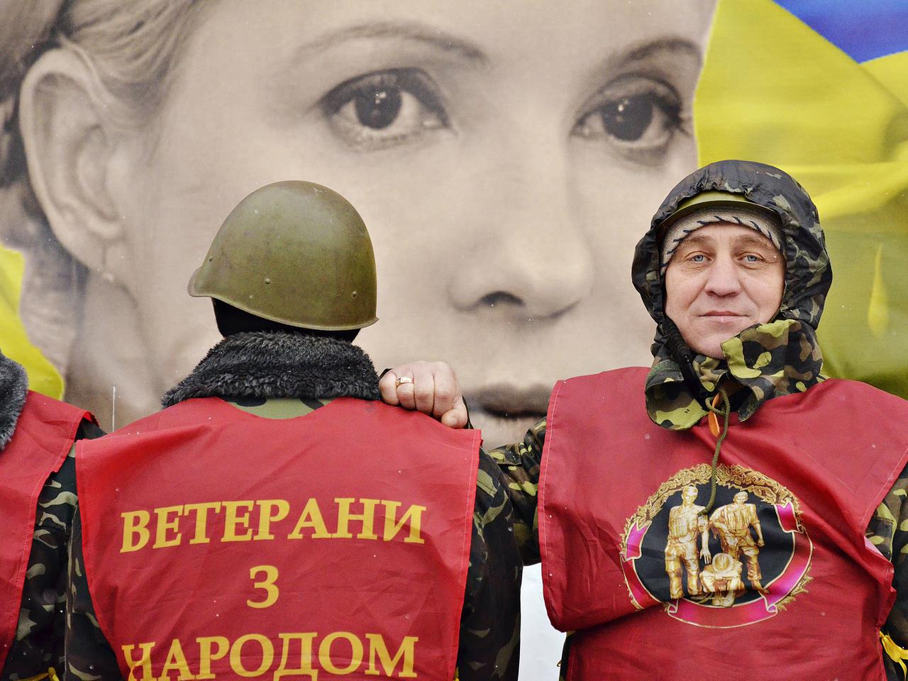 Ein Plakat der ukrainischen Oppositionspolitikerin Julia Timoschenko, davor zwei Personen auf dem Unabhängigkeitsplatz in Kiew