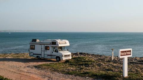 Ein Camper-Van steht auf einem Parkplatz am Meer.