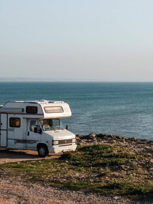 Ein Camper-Van steht auf einem Parkplatz am Meer.