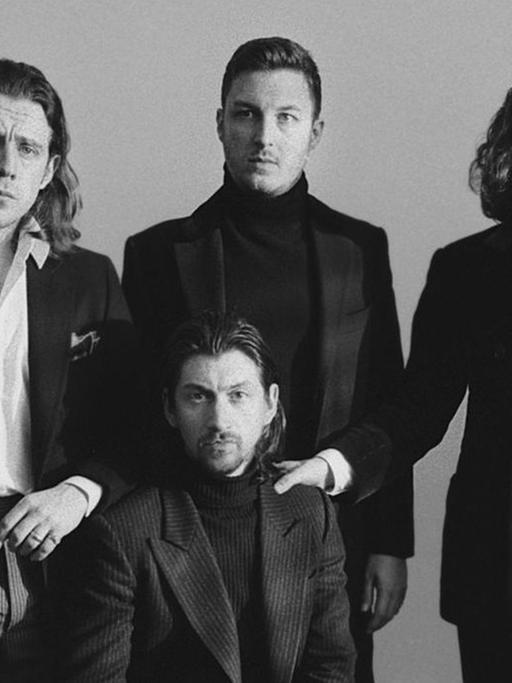 Ein Schwarzweiß-Foto der Band Arctic Monkeys. Die Band trägt gediegene Kleidung und macht damit einen sehr edlen Eindruck.