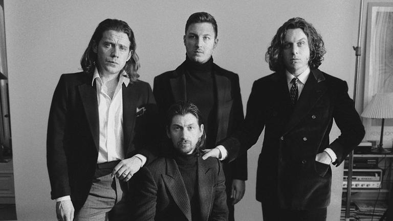 Ein Schwarzweiß-Foto der Band Arctic Monkeys. Die Band trägt gediegene Kleidung und macht damit einen sehr edlen Eindruck.