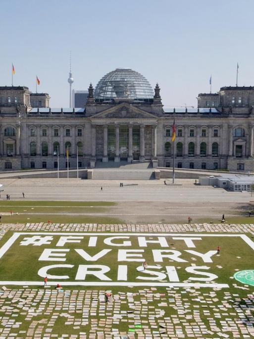 Zahlreiche Protestschilder liegen auf der Wiese vor dem Bundestag – dazwischen steht "#Fight Every Crisis".