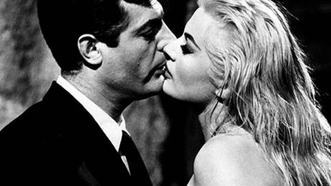 Großaufnahme in Schwarzweiß von Marcello Mastroianni und Anita Ekberg, die in einem Stadtbrunnen stehen und sich küssen.