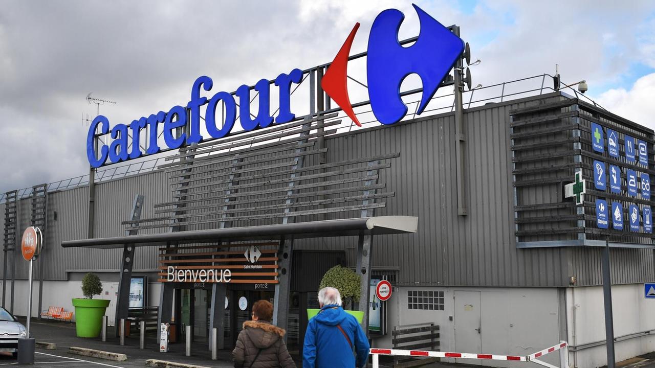 Menschen gehen über einen Parkplatz auf einen großen Carrefour-Supermarkt in Frankreich zu.