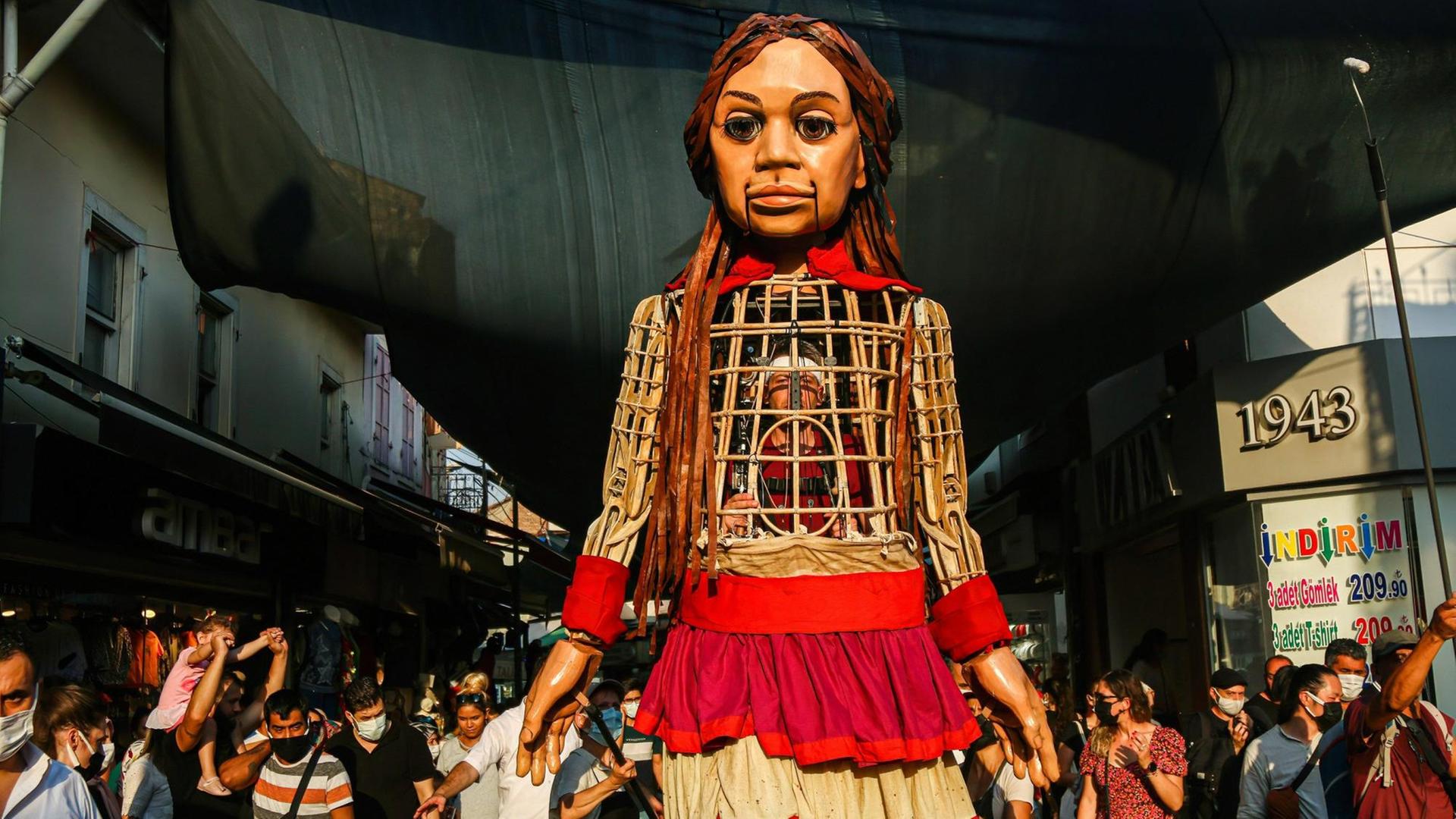 Die 3,5 Meter große Puppe "Amal" läuft durch die Straßen desr türkischen Stadt Izmir. Sie ist ein Teil der Kunstaktion "The Walk", in Gaziantepp gestartet und wird vier Monate lang 8.000 Kilometer gehen sowie acht Ländergrenzen der EU passieren. Dabei soll sie auf alle Herausforderungen aufmerksam machen, die syrische geflüchtete Kinder meistern müssen.