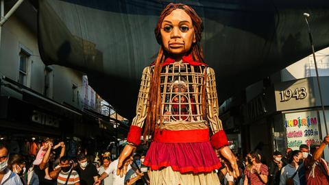 Die 3,5 Meter große Puppe "Amal" läuft durch die Straßen desr türkischen Stadt Izmir. Sie ist ein Teil der Kunstaktion "The Walk", in Gaziantepp gestartet und wird vier Monate lang 8.000 Kilometer gehen sowie acht Ländergrenzen der EU passieren. Dabei soll sie auf alle Herausforderungen aufmerksam machen, die syrische geflüchtete Kinder meistern müssen.