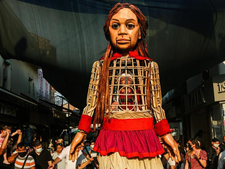 Die 3,5 Meter große Puppe "Amal" läuft durch die Straßen desr türkischen Stadt Izmir. Sie ist ein Teil der Kunstaktion "The Walk", in Gaziantepp gestartet und wird vier Monate lang 8.000 Kilometer gehen sowie acht Ländergrenzen der EU passieren. Dabei soll sie auf alle Herausforderungen aufmerksam machen, die syrische geflüchtete Kinder meistern müssen.