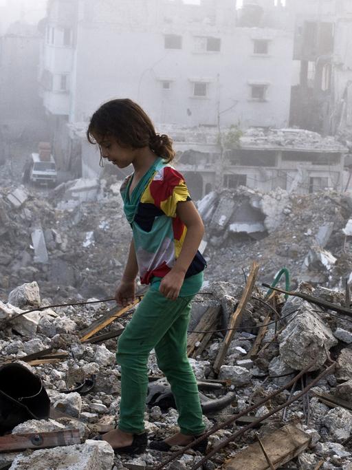 Ein Mädchen läuft über die Trümmer eines zerstörten Hauses.