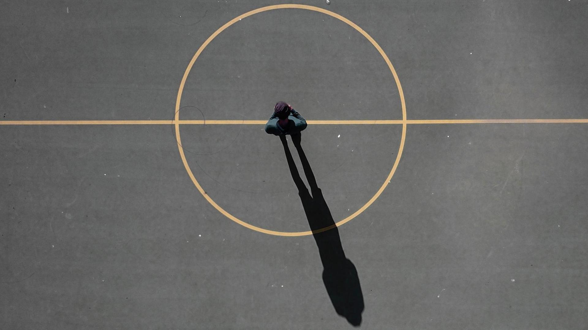 Ein Mann steht im Zentrum eines Spielfeldes, sein Schatten ragt aus dem Mittelkreis heraus.