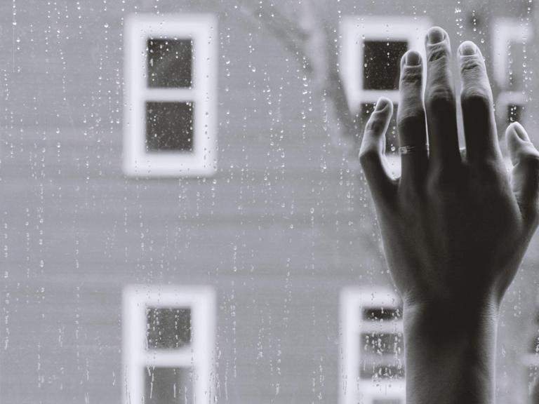 Eine Hand vor einem Fenster, dahinter Regen.