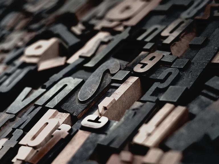 Einzelne, hölzerne Buchstaben liegen kreuz und quer bereit zum setzen der Texte im historischen Druckverfahren.