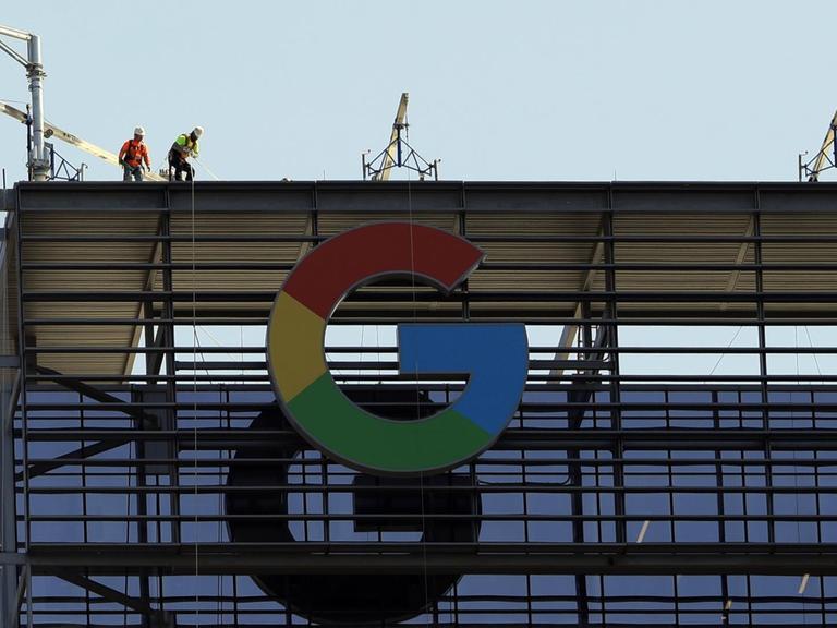 Bauarbeiter arbeiten auf einem Gebäude, an dem das große "G" für Google steht