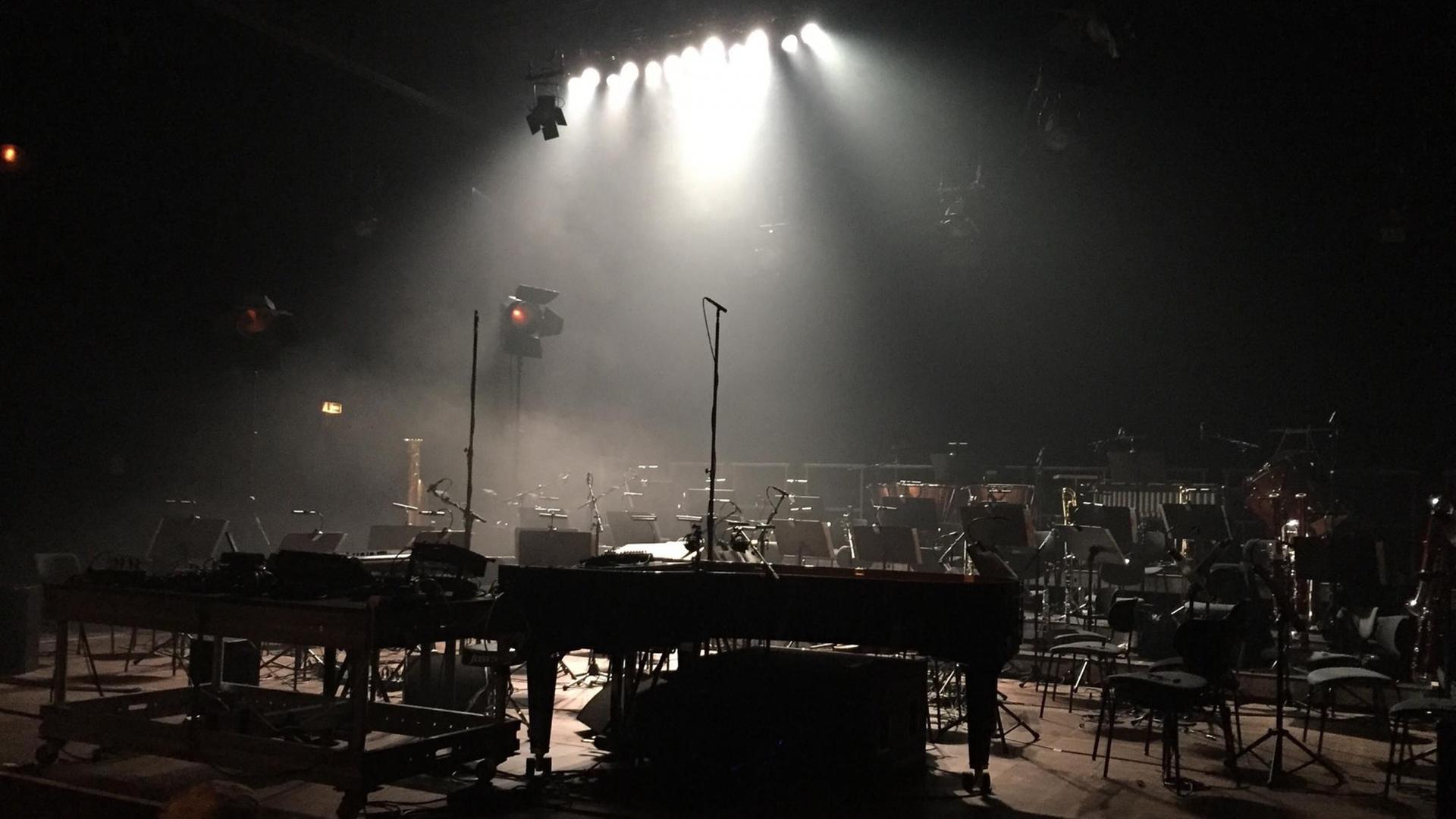 Ein Orchsteraufbau auf einer menschenleeren Bühne im Scheinwerferlicht. Stühle, ein Konzertflügel und andere Instrumente stehen bereit für ein Konzert.