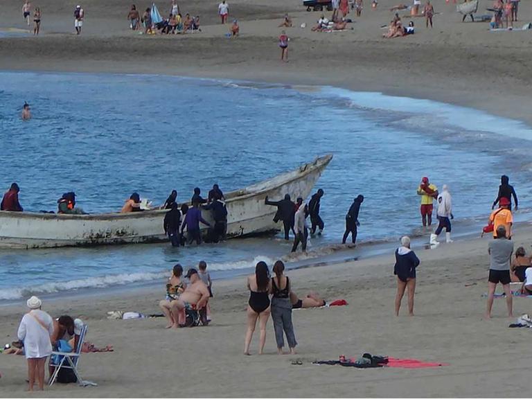 Flüchtlinge landen im Dezember in einem Boot am Strand von Los Cristianos auf der spanischen Insel Teneriffa. Dazwischen sind Touristen.