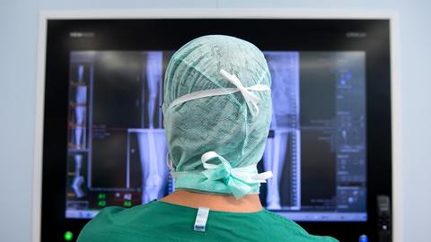 Ein Arzt schaut sich nach einer Knie-Operation in einem Operationssaal Röntgenbilder auf einem Monitor an.