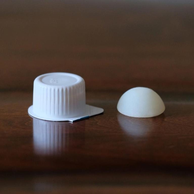 Das Foto zeigt links ein klassisches Milchdöschen in Plastikverpackung, recht daneben die auflösbare Milchkapsel