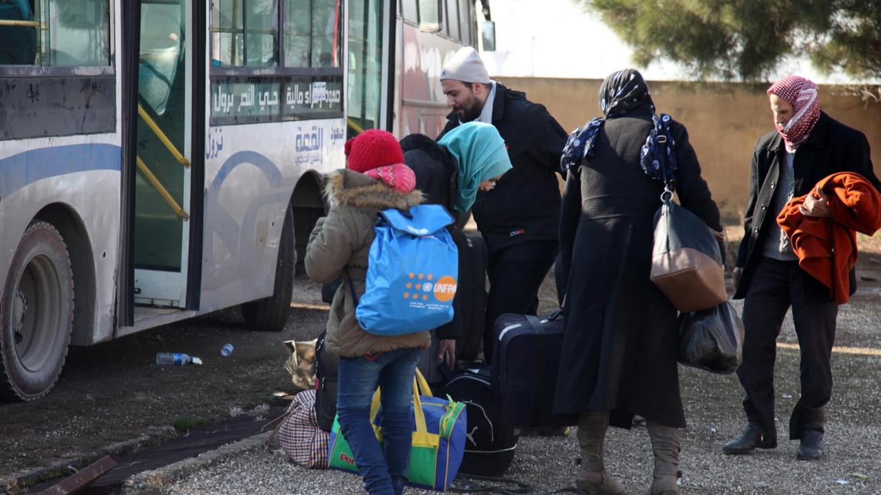 Eine syrische Familie mit Koffern und Taschen vor einem Bus,
