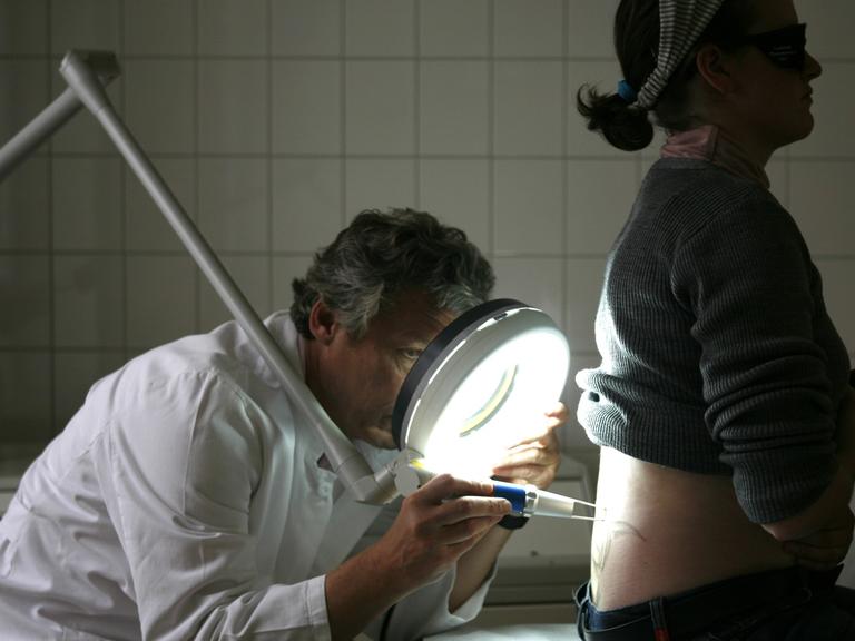 Ein Dermatologe entfernt mit einem Laser die Tätowierung einer Patientin.