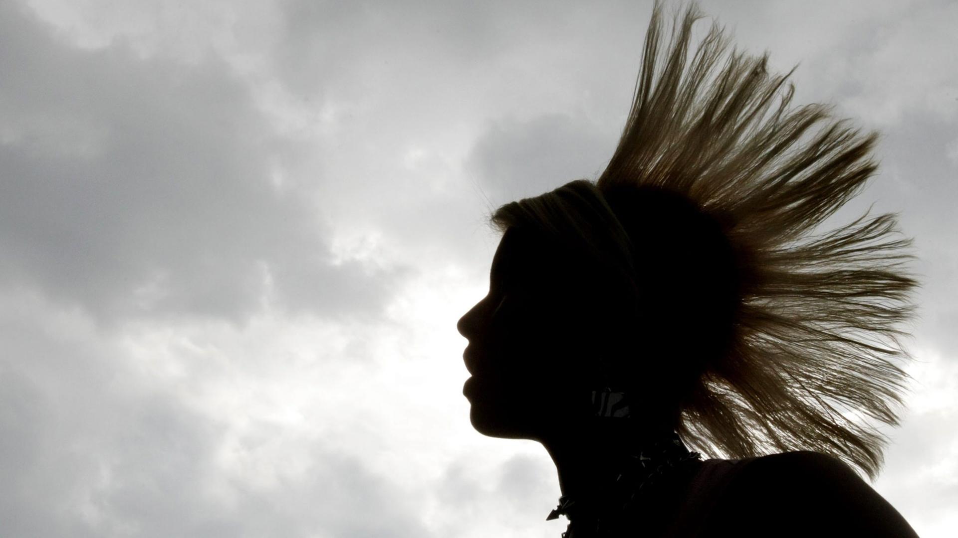 Eine Frau mit Irokesenschnitt im Profil vor grauem Himmel