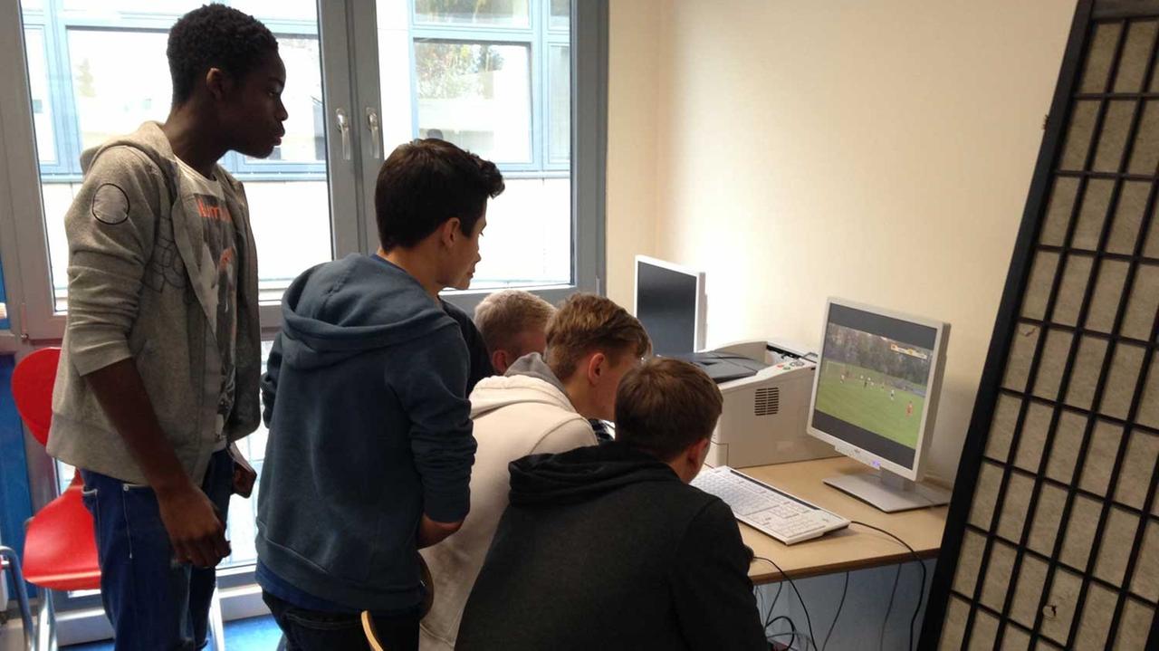 Eine Gruppe Schüler hat sich um einen PC in der Geißbockakademie versammelt und schaut sich ein Spiel vom vergangenen Wochenende an.
