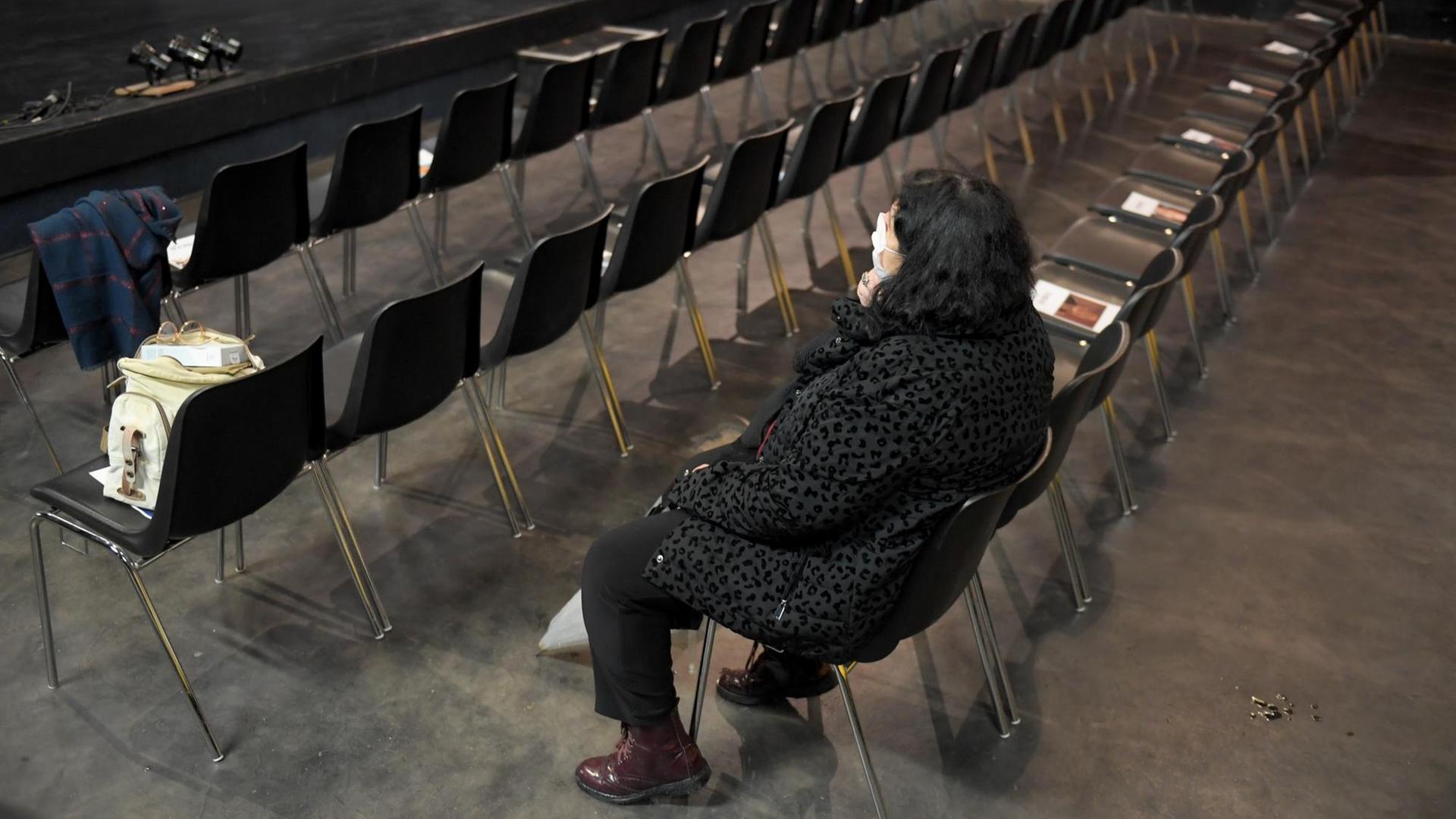 Eine Frau sitzt im Zuschauerraum eines leeren Theaters.