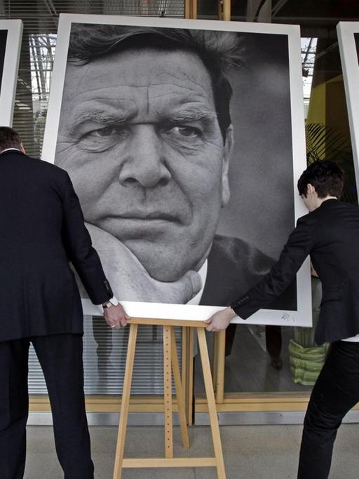 Die Portraits von Angela Merkel, Gerhard Schröder und Helmut Kohl werden aufgerichtet.