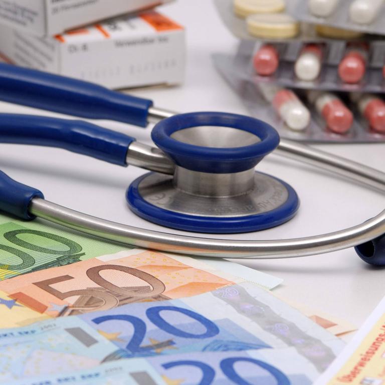 Stethoskop, Geldscheine, Überweisung und Medikamente auf einem Tisch in Großaufnahme