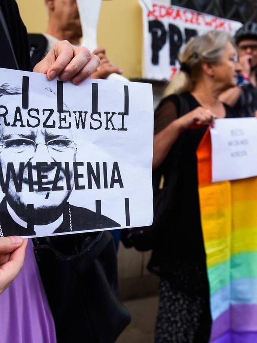 Eine Frau hält bei einer Demonstration in Krakau am 4. August 2019 ein Plakat, auf dem steht: "Jedraszewski ins Gefängnis". Menschen neben ihr halten eine Regenbogenfahne in die Höhe. Der Protest richtet sich gegen den Erzbischof von Krakau, Marek Jedraszewski, der die polnische LGBT-Bewegung mit einer Seuche verglichen hatte.