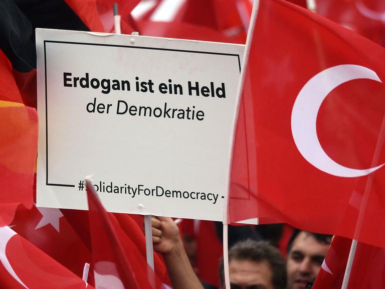 Anhänger des türkischen Staatspräsidenten Erdogan halten in Köln Fahnen. Einer hält ein Schild hoch mit der Aufschrift "Erdogan ist ein Held der Demokratie".