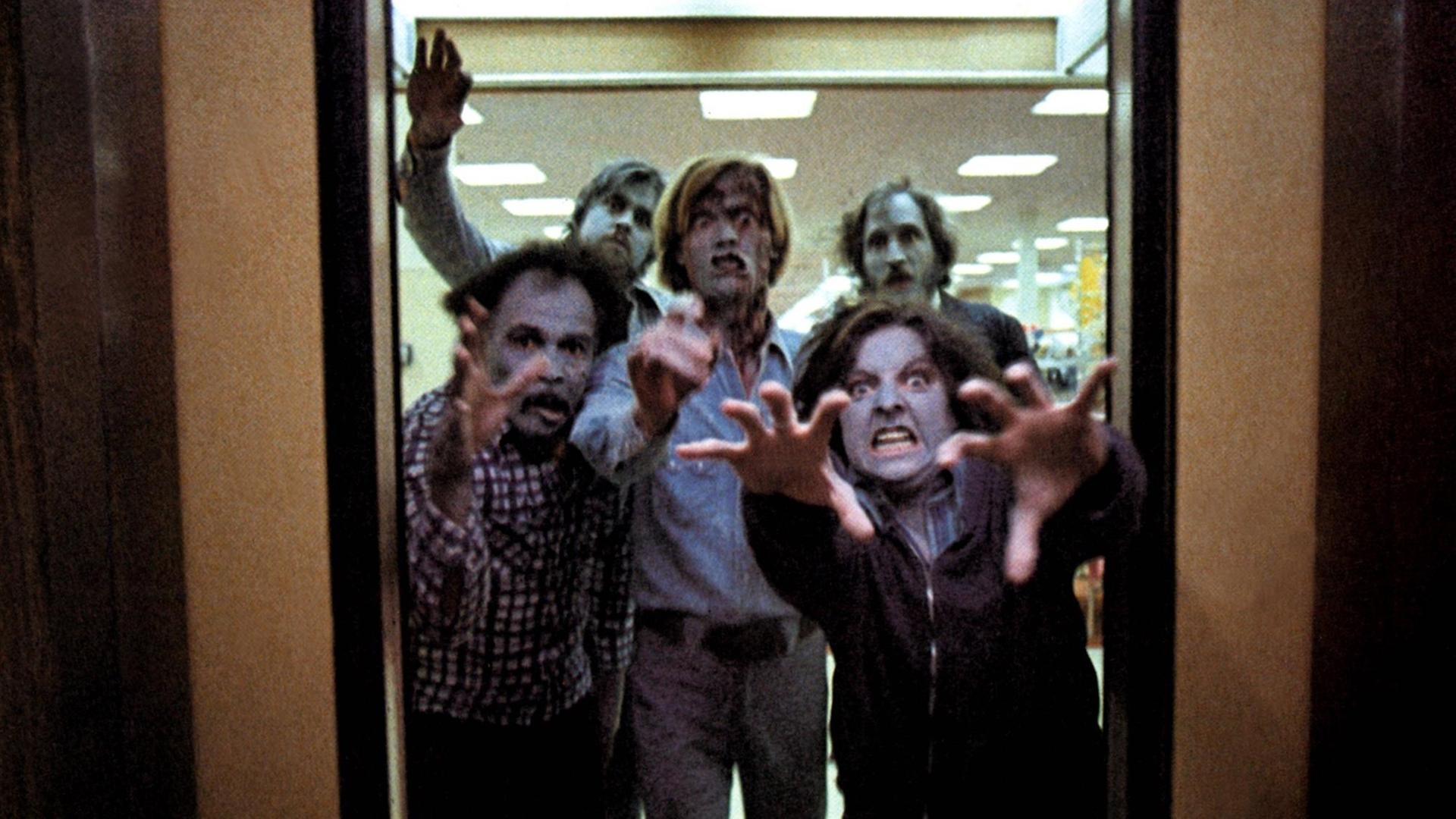 Zombies stürmen durch eine Tür in Richtung Kamera und greifen scheinbar mit den Händen nach dem Betrachter
