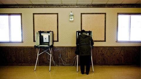 Zwei Wahlkabinen, in einer steht eine Frau.
