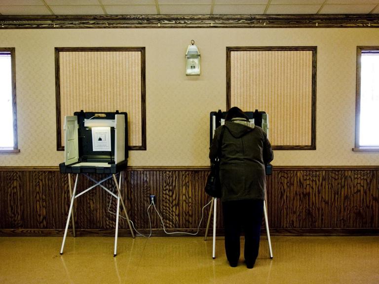 Zwei Wahlkabinen, in einer steht eine Frau.