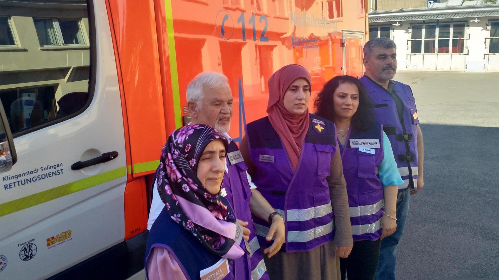 Die muslimische Notfallbegleiter aus Solingen stehen in violetten Westen vor einem Rettungswagen