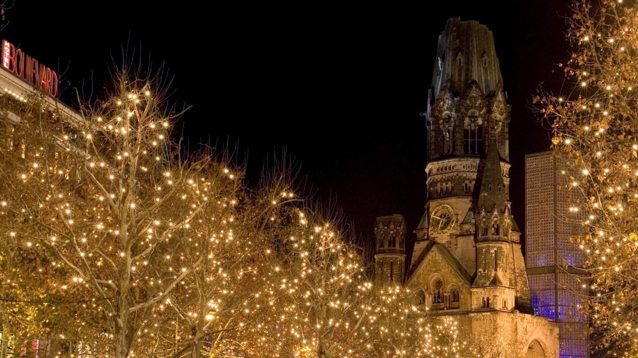 Mit vielen kleinen Lichtern geschmückte Bäume am weihnachtlichen Kurfürstendamm vor der Kaiser-Wilhelm-Gedächtniskirche in Berlin.