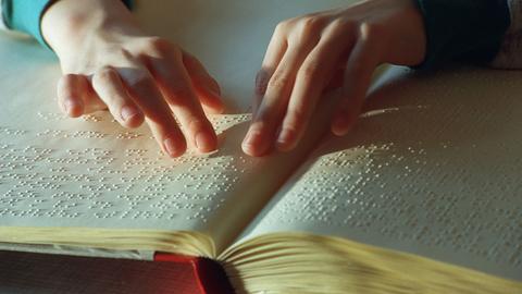 Eine Hand fährt über einen Text in Brailleschrift.