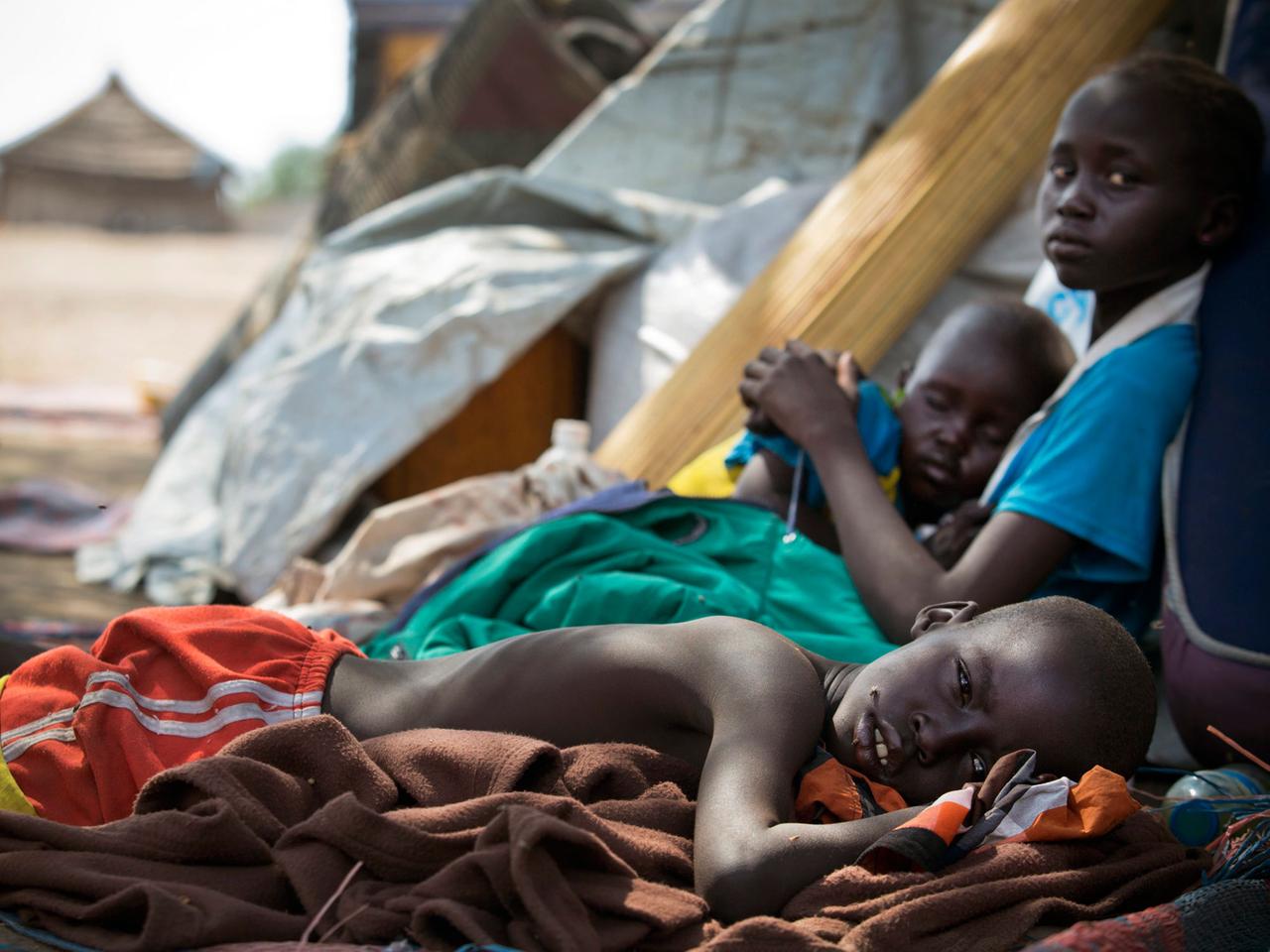 Ein Foto des Kinderhilfswerks UNICEF zeigt drei Kinder in der südsudanesischen Stadt Mingkaman, während sie erschöpft darauf warten, als Hilfesuchende registriert zu werden.