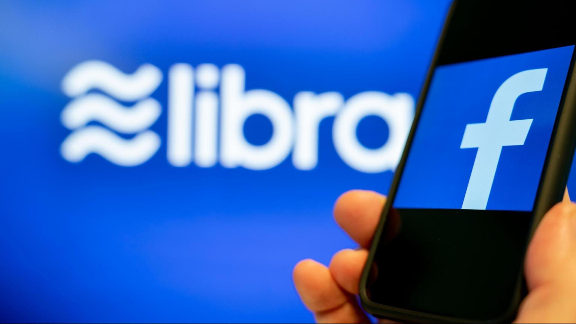Ein Smartphone mit Facebook-Logo auf dem Display wird neben ein Logo von Libra gehalten.