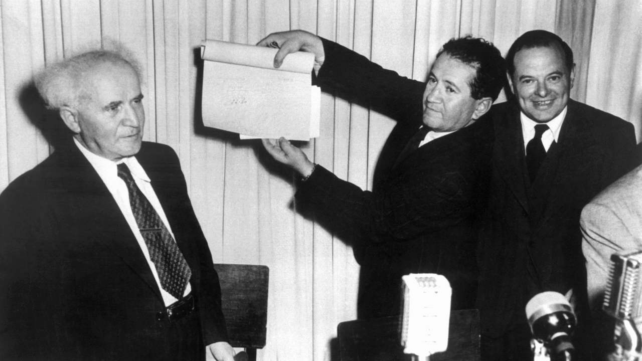 Nach der Unterzeichnung der Proklamationsurkunde am 14. Mai 1948 im Stadtmuseum von Tel Aviv hält eine nicht identifizierte Person das Schriftstück mit den Unterschriften in die Höhe, links David Ben Gurion, der erste Ministerpräsident Israels.