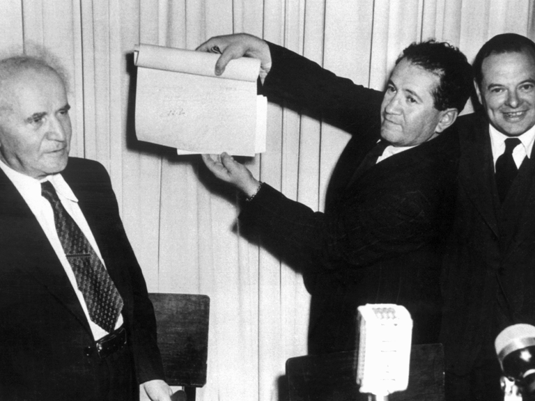 Nach der Unterzeichnung der Proklamationsurkunde am 14. Mai 1948 im hält eine nicht identifizierte Person das Schriftstück in die Höhe. Links: David Ben Gurion, der erste Ministerpräsident Israels.