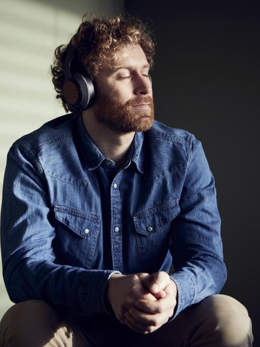 Ein Mann mit geschlossenen Augen hört über Kopfhörer Musik