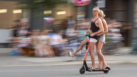 Ein Paar fährt zu zweit fährt mit einem E-Scooter auf der Strasse durch Berlin.