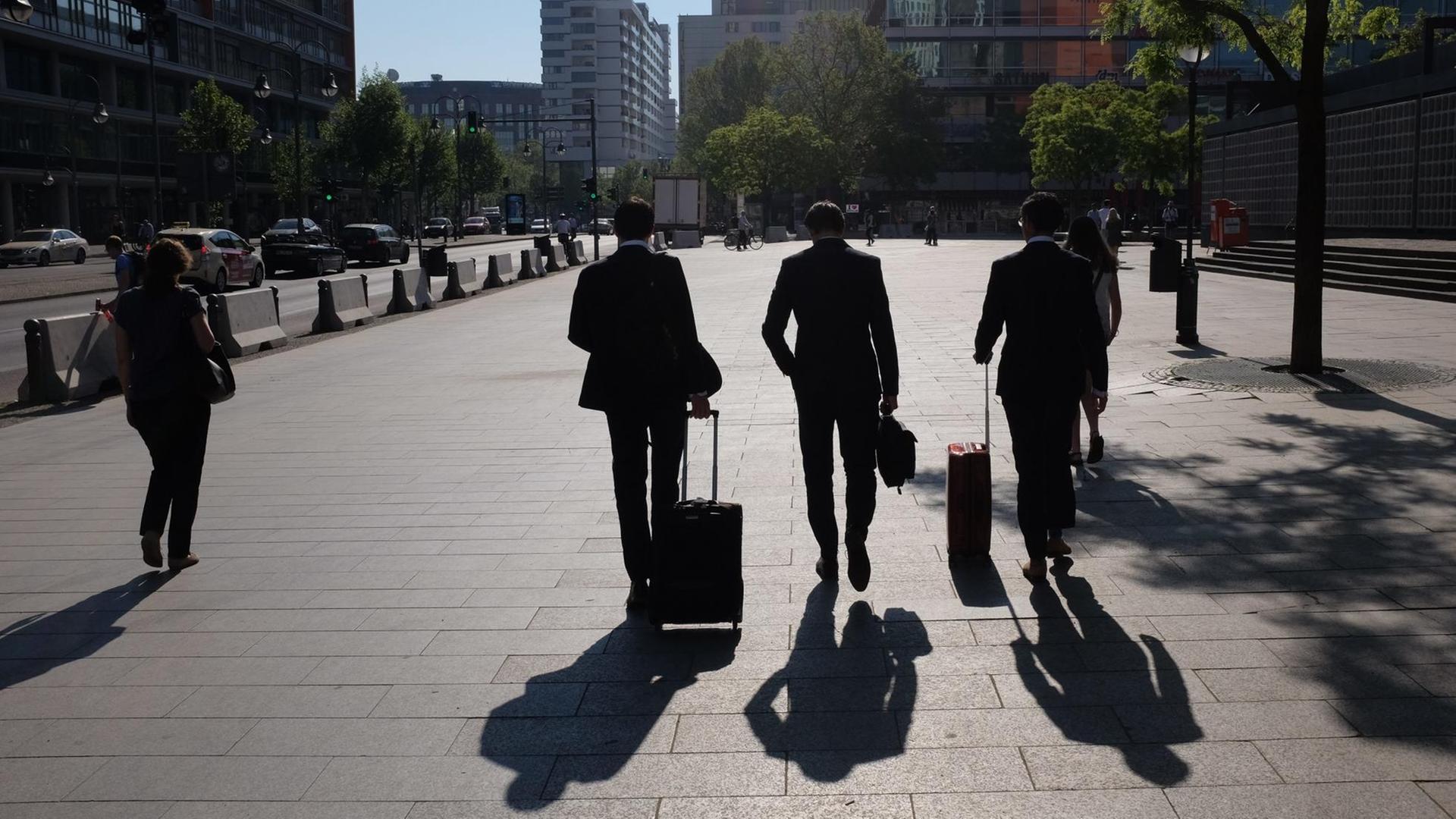Die Schatten dreier Geschäftsleute, die mit ihren Rollkoffern zu einem Termin eilen.
