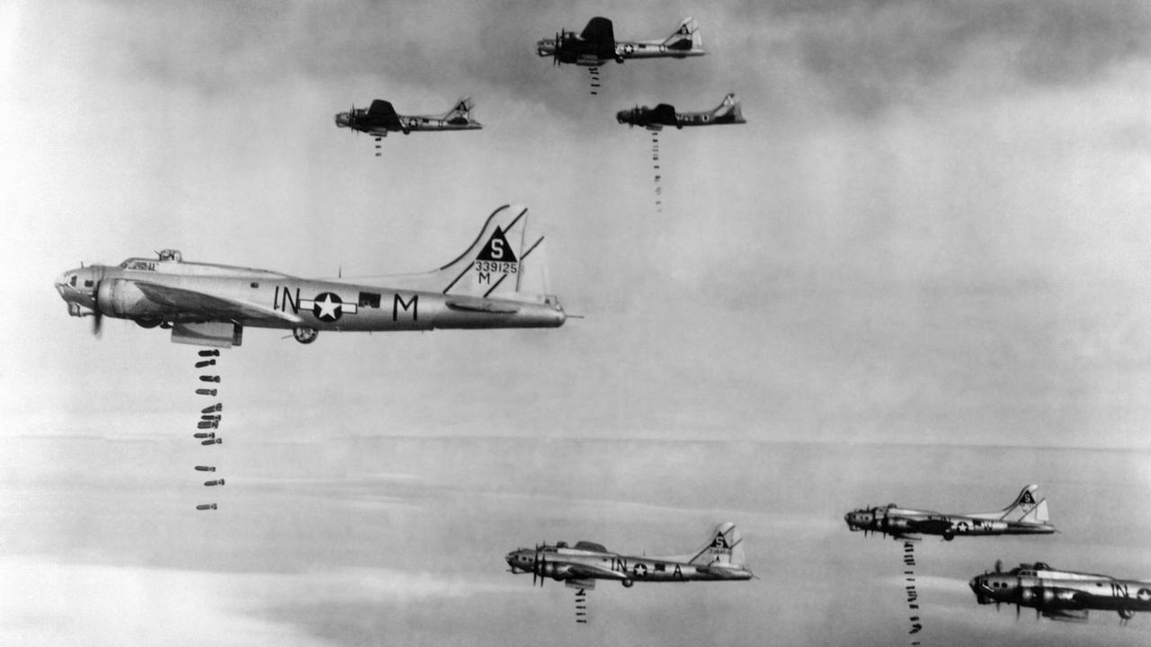 Das Foto zeigt amerikanische Bomber im 2. Weltkrieg am Himmel. Aus den Flugzeugen fallen unten Bomben heraus.