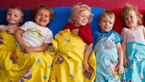 Fünf Kinder liegen lächelnd und zugedeckt, gemeinsam auf Matratzen.